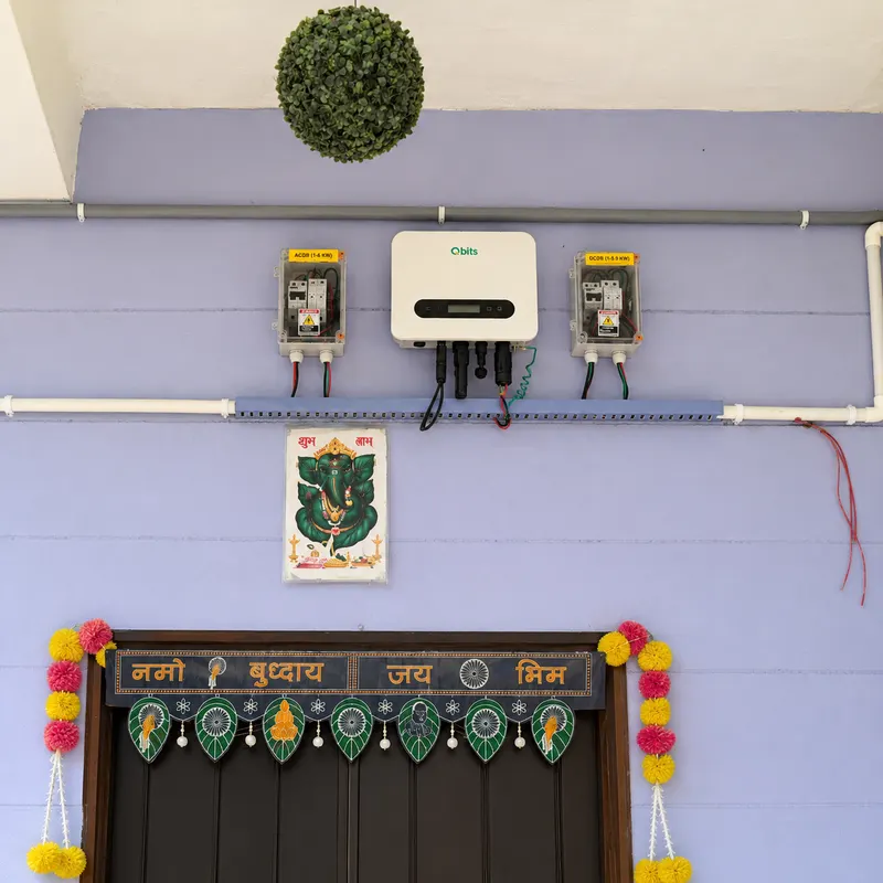 Qbits solar inverter mounted above a decorated home entrance with marigold garlands and a toran